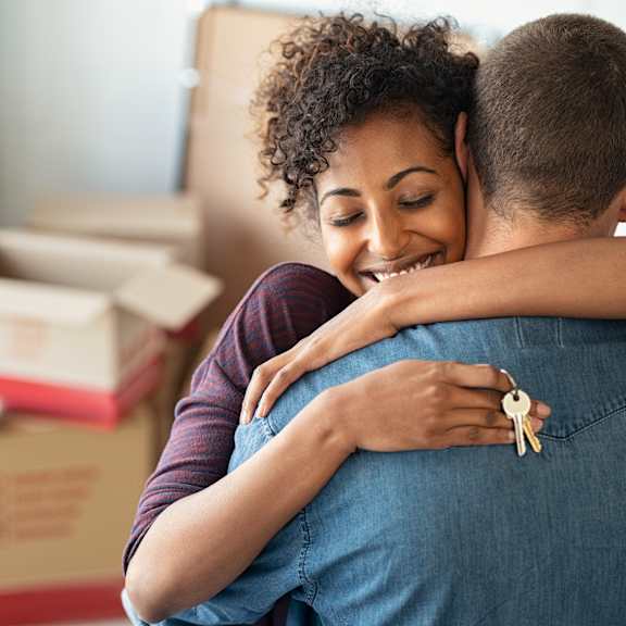 a couple hugging each other in a room with boxes in the background.