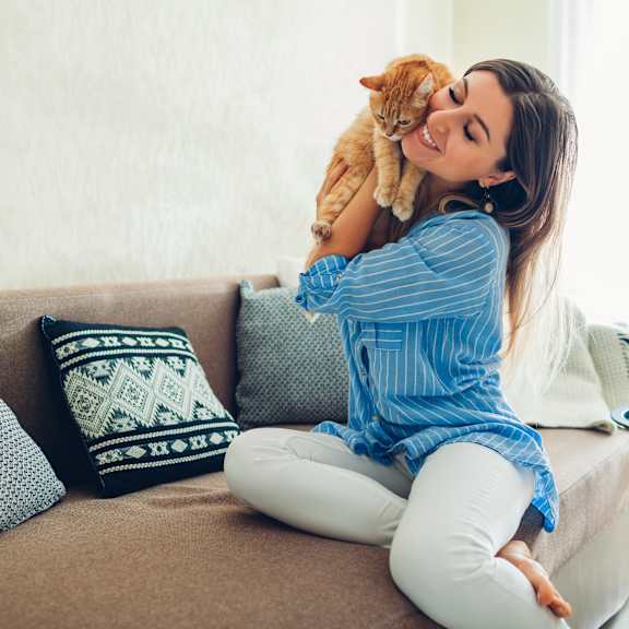 a woman in a blue striped shirt is sitting on a couch holding a cat.