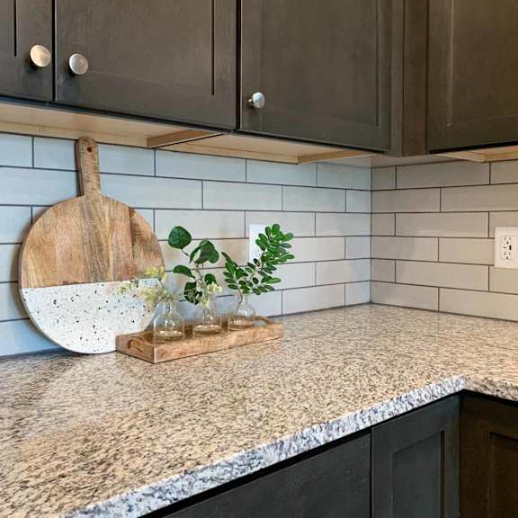 Thumbnail 6 of 22 a corner of the kitchen with dark cabinets, a white tile backsplash, and a decorative cutting board
