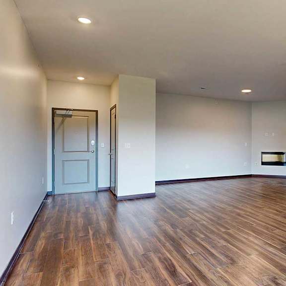 Thumbnail 5 of 26 A living room with wooden flooring and an electric fireplace next to a front entryway with a coat closet.
