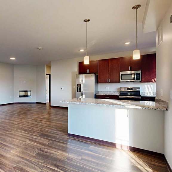Thumbnail 20 of 26 A living room with wooden flooring, next to an open kitchen with dark wooden cabinets and a peninsula counter.