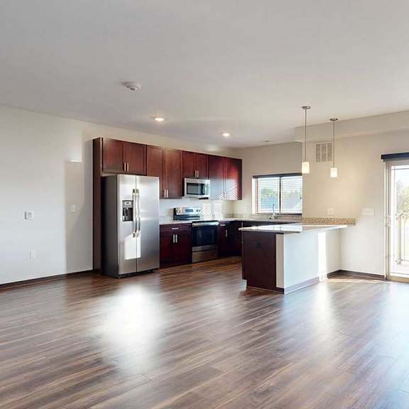 Thumbnail 19 of 26 A living room with hardwood flooring, next to an open modern kitchen with dark wooden cabinets, and a sliding glass door to a balcony.