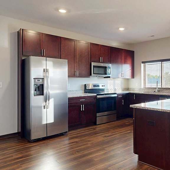 Thumbnail 15 of 26 A modern kitchen with dark wooden cabinets, granite countertops, stainless steel appliances, a large window over the sink, and a peninsula counter.