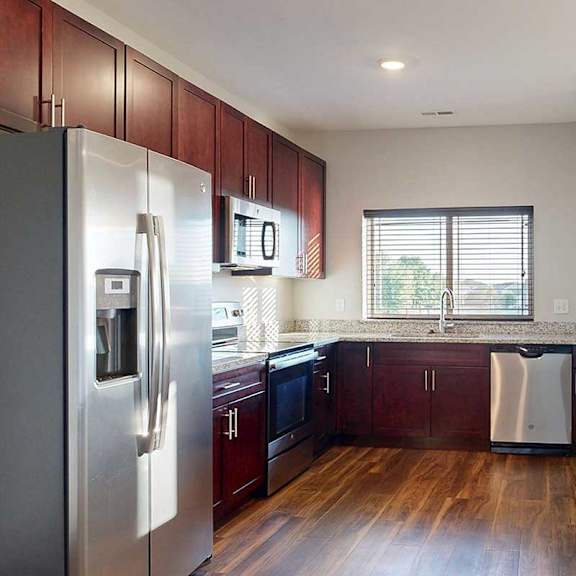 Thumbnail 10 of 26 A modern kitchen with dark wooden cabinets, granite countertops, stainless steel appliances, a large window over the sink, and a peninsula counter.