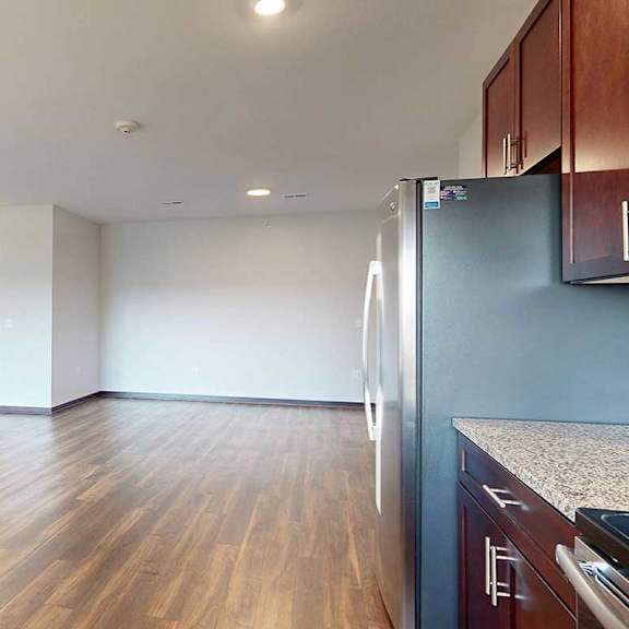 Thumbnail 13 of 26 A modern kitchen with dark wooden cabinets, opens up to a living room with hardwood flooring.