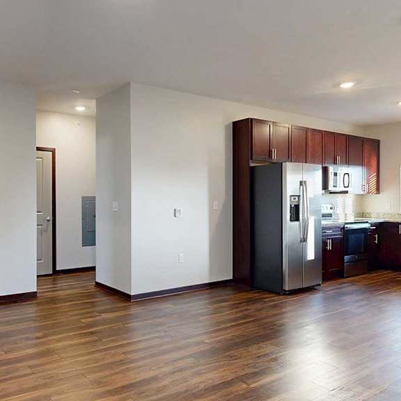 Thumbnail 8 of 26 A living room with hardwood flooring and an electric fireplace, next to an open modern kitchen with dark wooden cabinets.