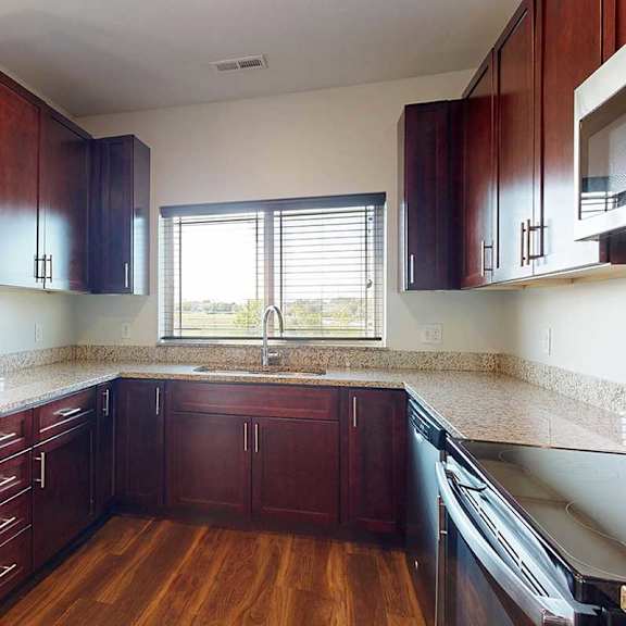 Thumbnail 10 of 29 A modern kitchen with dark wooden cabinets, granite countertops, stainless steel appliances, a large window over the sink, and a peninsula counter.