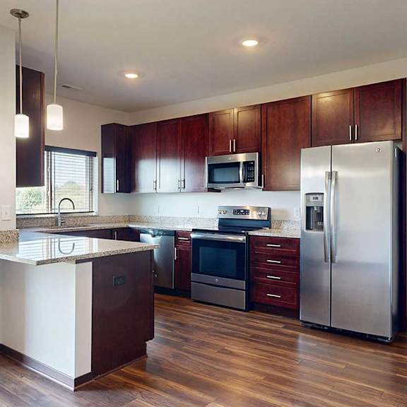 Thumbnail 7 of 29 A modern kitchen with dark wooden cabinets, granite countertops, stainless steel appliances, a large window over the sink, and a peninsula counter.