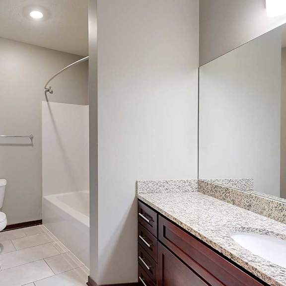 Thumbnail 30 of 34 A long bathroom with a granite vanity sink, mirror, and tub shower.