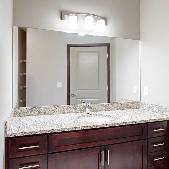 Thumbnail 29 of 34 A bathroom with a granite vanity sink, an oversized mirror, and overhead lighting.