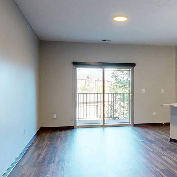 Thumbnail 18 of 34 An open-concept living room with hardwood flooring and a sliding glass door to a balcony, that connects to a modern kitchen with a large central island.