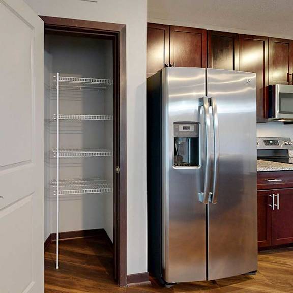 Thumbnail 17 of 34 A kitchen pantry with built-in corner shelves next to a stainless steel fridge.