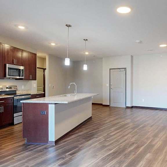 Thumbnail 22 of 34 An open-concept living room with hardwood flooring and an electric fireplace, that connects to a modern kitchen with a large central island.