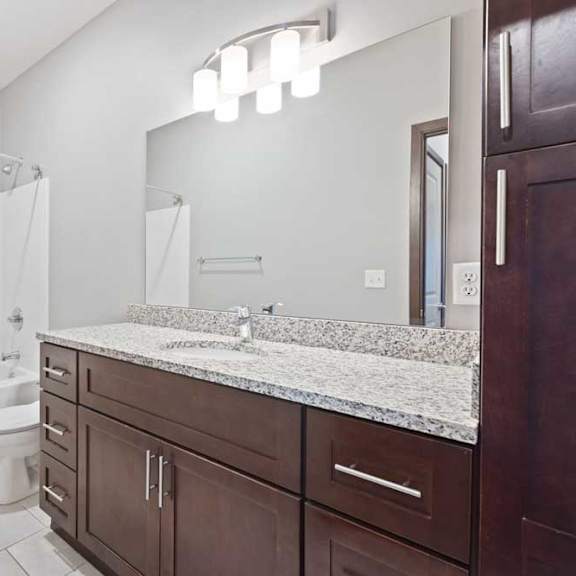 Thumbnail 14 of 15 A bathroom with a granite vanity, dark wooden cabinets, and a tub shower.