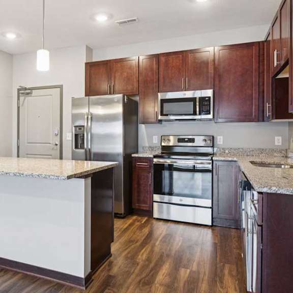 Thumbnail 3 of 15 A kitchen with dark wood cabinets, granite countertops, a large island, and stainless steel appliances.