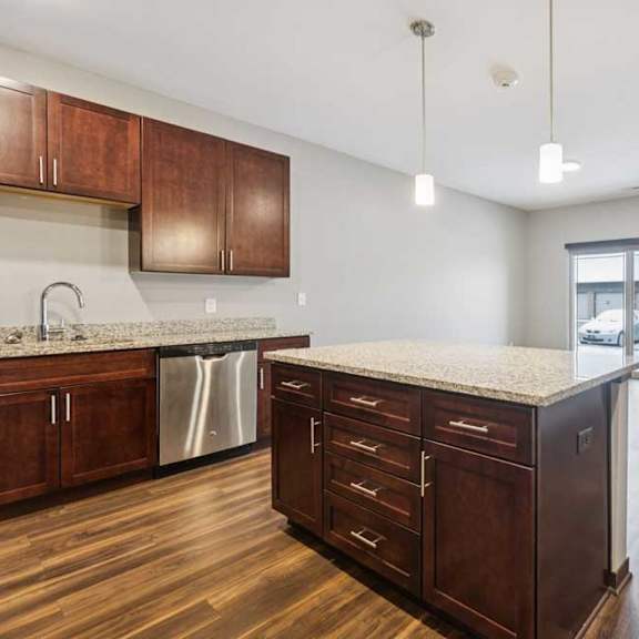 Thumbnail 5 of 15 A kitchen with dark wooden cabinets and a large island, in front of a spacious living room.