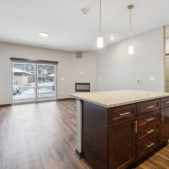 Thumbnail 6 of 15 A kitchen with dark wooden cabinets and a large island, in front of a spacious living room.