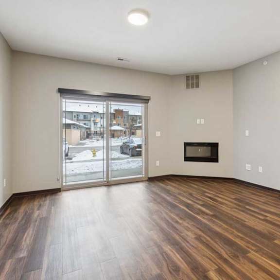 Thumbnail 7 of 15 A living room with hardwood-style flooring, an electric fireplace, and a sliding glass door to a patio.