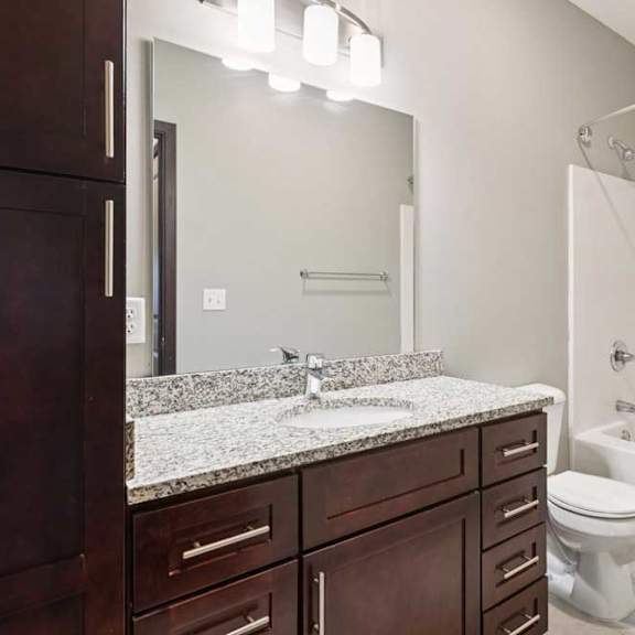 Thumbnail 17 of 18 A bathroom with a granite vanity, dark wooden cabinets, and a tub shower.