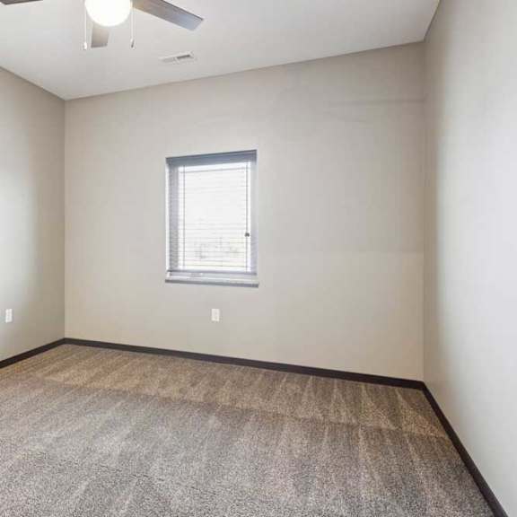 Thumbnail 14 of 18 A carpeted bedroom with a ceiling fan and a window.