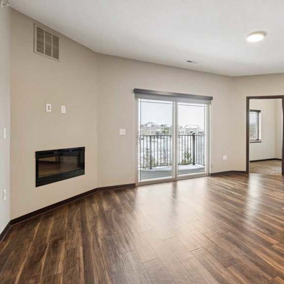 Thumbnail 8 of 18 A living room with hardwood-style flooring, an electric fireplace, and a sliding glass door to a balcony.