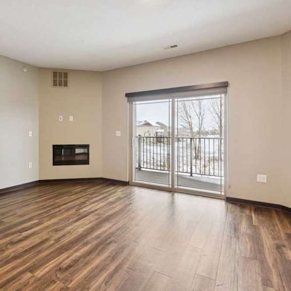 Thumbnail 11 of 18 A living room with hardwood-style flooring, an electric fireplace, and a sliding glass door to a balcony.
