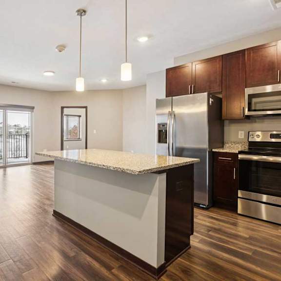Thumbnail 7 of 18 A kitchen with dark wooden cabinets and a large island, in front of a spacious living room.