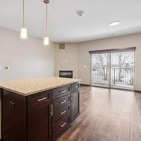 Thumbnail 6 of 18 A kitchen with dark wooden cabinets and a large island, in front of a spacious living room.