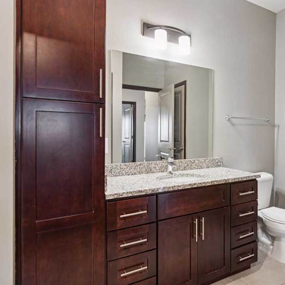 Thumbnail 31 of 34 A bathroom with a granite vanity, dark wooden cabinets, and a large mirror with overhead lighting.