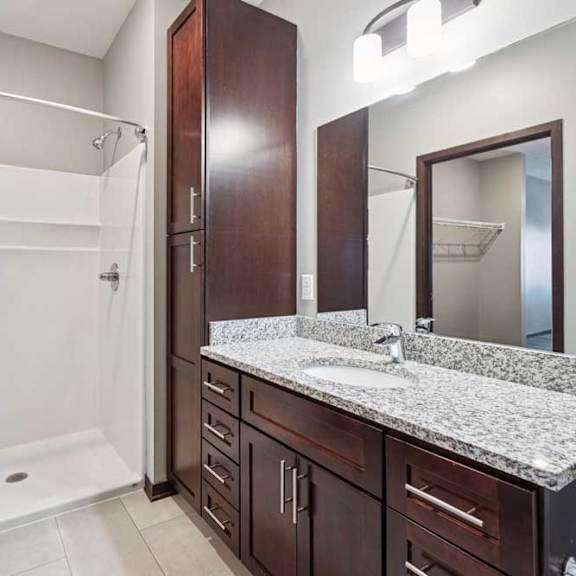 Thumbnail 32 of 34 A bathroom with a granite vanity, dark wooden cabinets, and a walk-in shower.