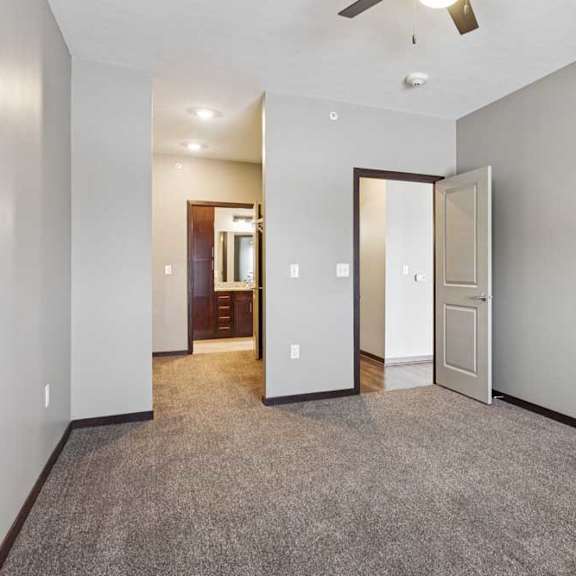 Thumbnail 29 of 34 A carpeted bedroom with a ceiling fan and an open walk-through closet to a connected bathroom.