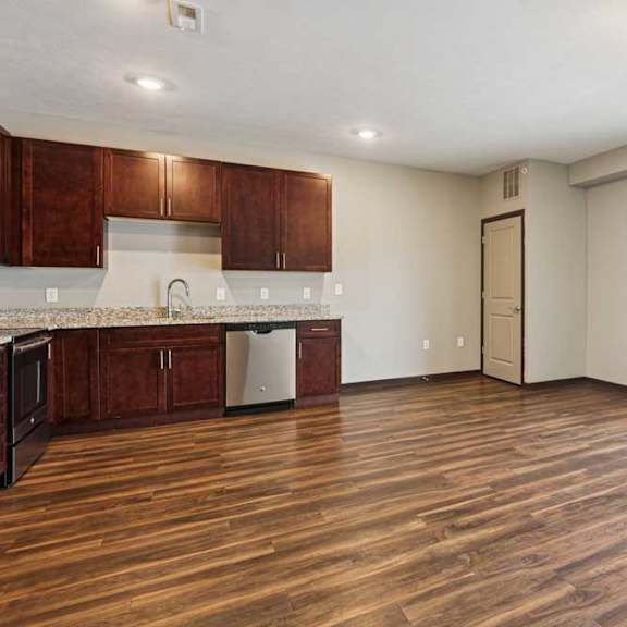 Thumbnail 22 of 34 A living room with hardwood-style flooring and kitchen with dark wooden cabinets.
