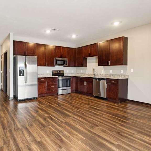 Thumbnail 20 of 34 A living room with hardwood-style flooring and kitchen with dark wooden cabinets.