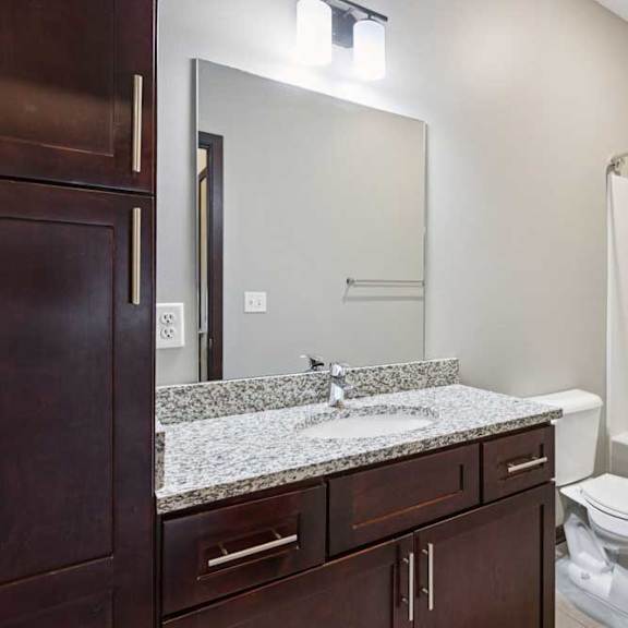 Thumbnail 22 of 23 A bathroom with a granite vanity, dark wooden cabinets, and a tub shower.
