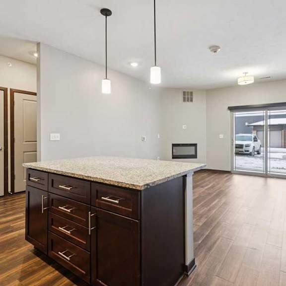 Thumbnail 16 of 23 A kitchen with dark wooden cabinets and a large island, in front of a spacious living room.