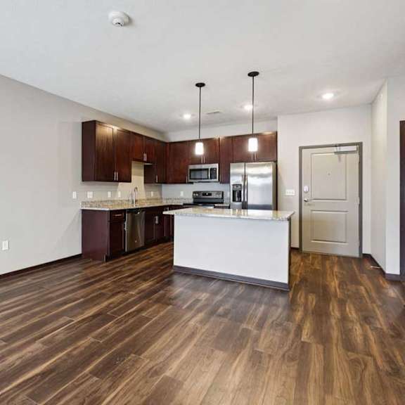 Thumbnail 18 of 23 A living room with hardwood-style flooring and kitchen with dark wooden cabinets.