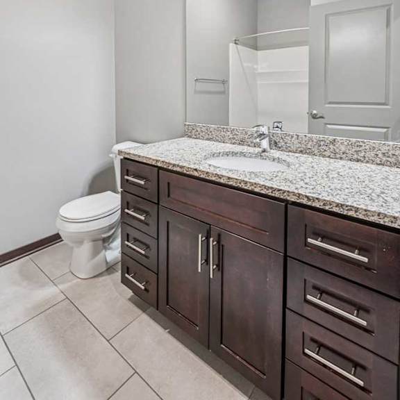 Thumbnail 14 of 15 A bathroom with a granite vanity, dark wooden cabinets, and a walk-in shower.