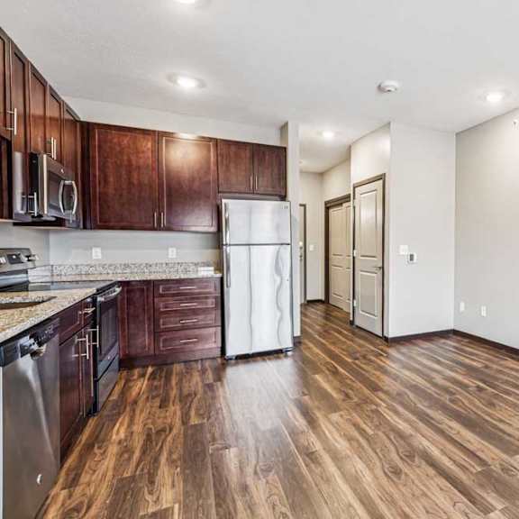 Thumbnail 4 of 15 A kitchen with dark wood cabinets and stainless steel appliances, open to a living area with hardwood-style flooring.