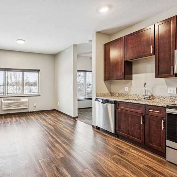 Thumbnail 8 of 15 A kitchen with dark wood cabinets and stainless steel appliances, open to a living area with a large window.