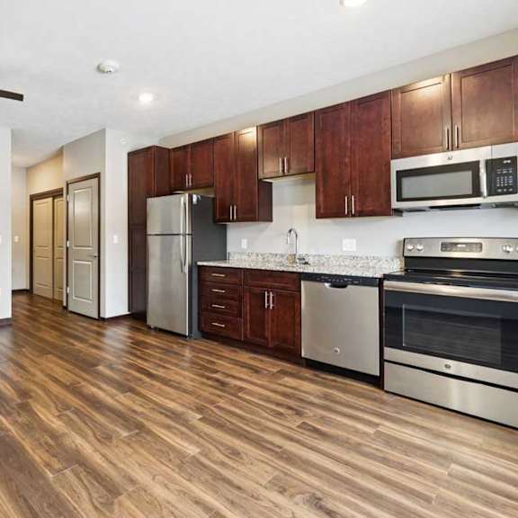 Thumbnail 5 of 11 A living area with a ceiling fan, open to a kitchen with dark wooden cabinets.