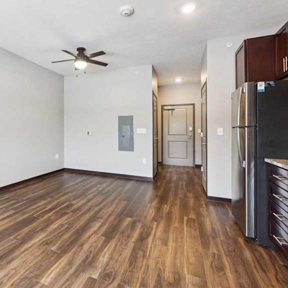 Thumbnail 9 of 11 A living area with a ceiling fan, open to a kitchen with dark wooden cabinets.