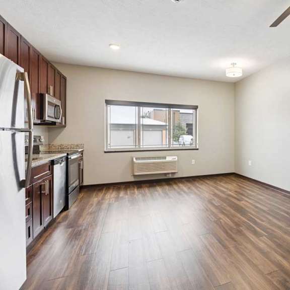 Thumbnail 8 of 11 A living area with a ceiling fan, open to a kitchen with dark wooden cabinets.