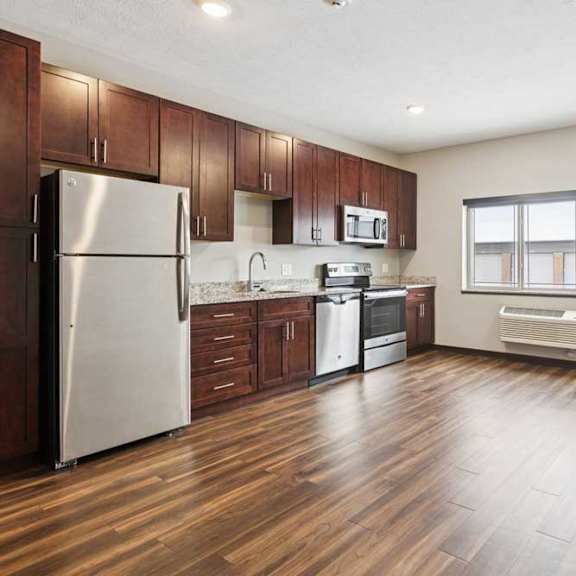 Thumbnail 7 of 11 A living area with a three-panel window, open to a kitchen with dark wooden cabinets.