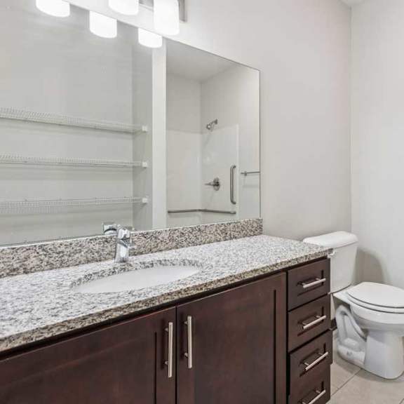 Thumbnail 14 of 21 A bathroom with a granite vanity, dark wooden cabinets, and a walk-in shower.