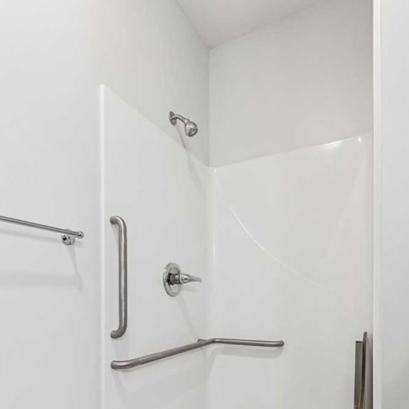 Thumbnail 15 of 21 A bathroom with a walk-in shower with a grab bar and fold out seat.