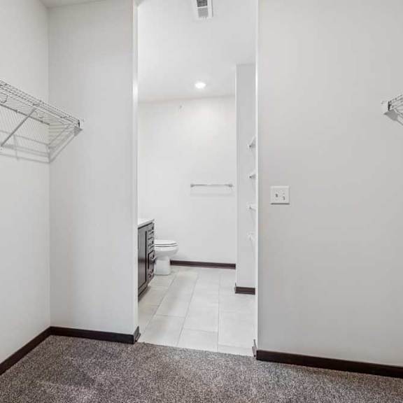 Thumbnail 13 of 21 An oversized walk-in closet with several built-in wire shelves connected to an ensuite bathroom.
