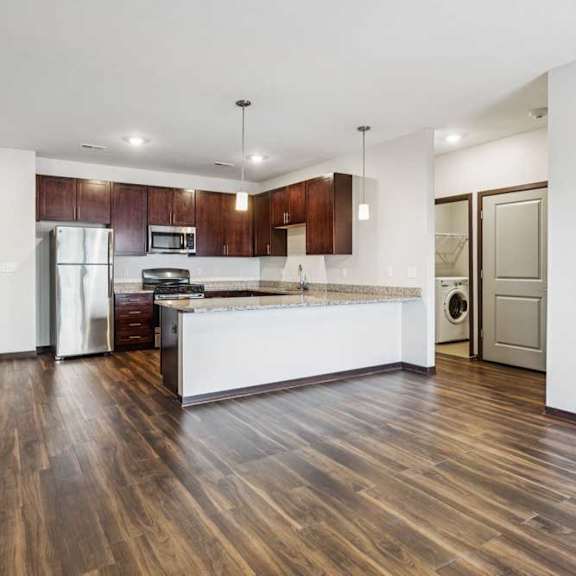 Thumbnail 16 of 21 A living room with hardwood-style flooring and kitchen with dark wooden cabinets.