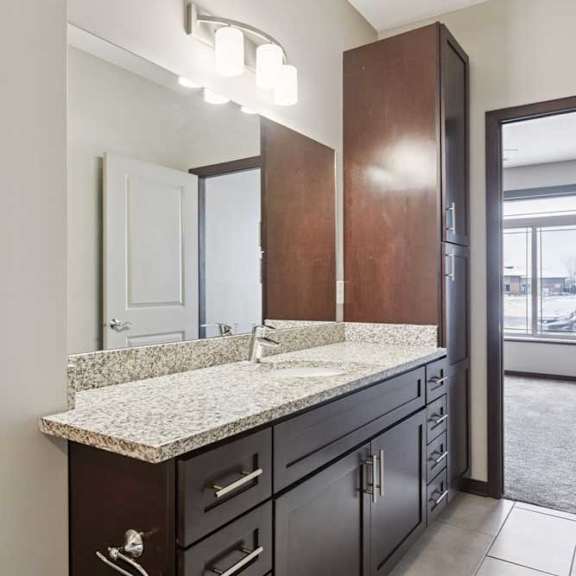 Thumbnail 14 of 19 A bathroom with a granite vanity, dark wooden cabinets, and a large mirror with overhead lighting.
