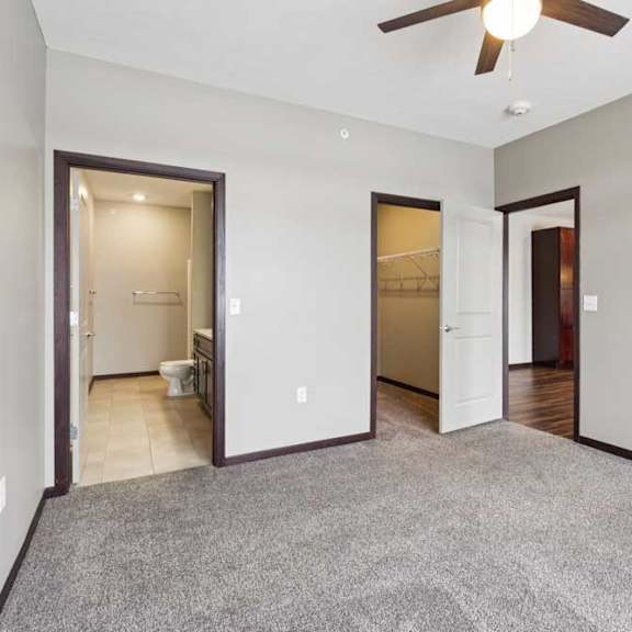Thumbnail 11 of 19 A carpeted bedroom with a ceiling fan, an attached bathroom, and an open walk-in closet.
