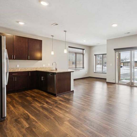 Thumbnail 9 of 19 A living room with hardwood-style flooring and kitchen with dark wooden cabinets.